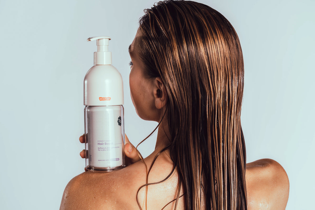 Iemand met nat haar houdt de navulbare fles WONDR Liquids conditioner vast